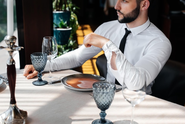 Um jovem empresário barbudo está sentado em uma mesa em um bom restaurante e esperando seu pedido atendimento ao cliente no catering