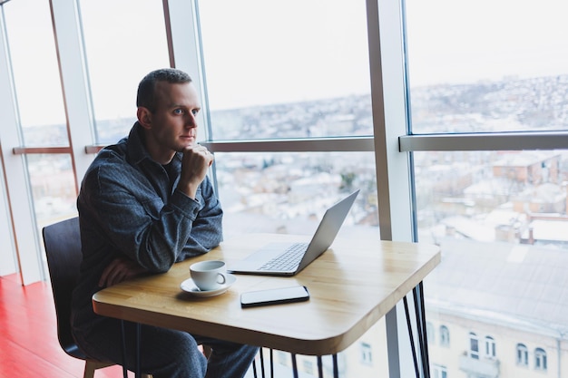 Um jovem empresário bem sucedido de terno bebe café e trabalha em um café com internet sem fio gratuita em um laptop sentado sozinho em uma mesa em um café