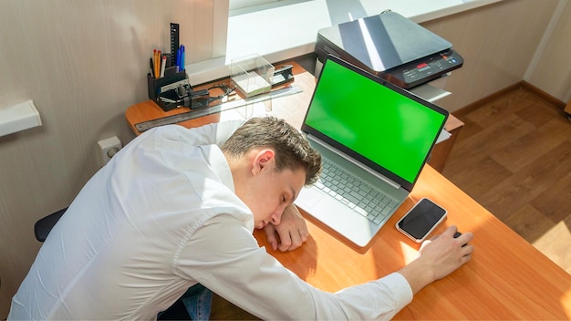 Um jovem empresário caucasiano cansado adormeceu em sua mesa no escritório em frente a um computador com