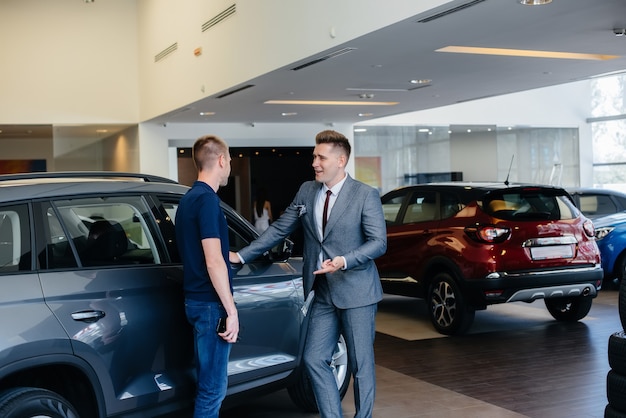 Um jovem empresário com um vendedor olha para um carro novo em uma concessionária. comprando um carro.