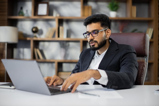 Um jovem empresário confiante do Oriente Médio sentado à mesa de trabalho em um escritório moderno falando com clientes