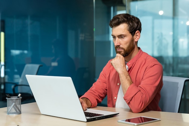 Um jovem empresário designer freelancer de camisa vermelha senta-se no escritório à mesa e trabalha em