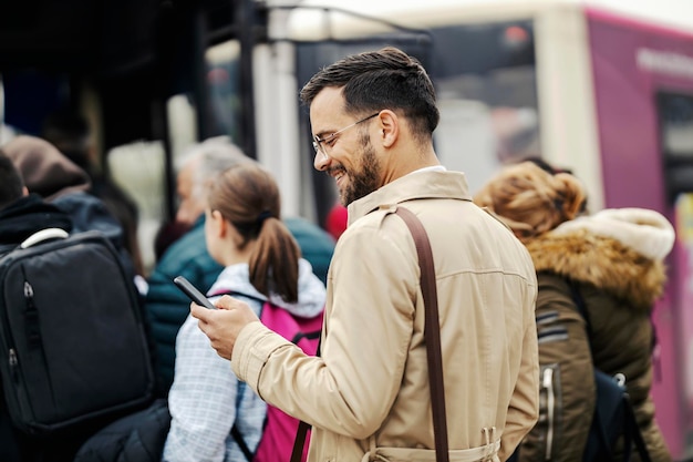 Um jovem empresário elegante está entrando no ônibus público e sorrindo para o telefone enquanto envia mensagens de texto