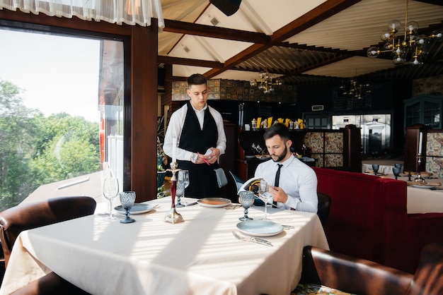 Um jovem empresário em um restaurante requintado examina o cardápio e faz um pedido para um jovem garçom com um avental estiloso. atendimento ao cliente.