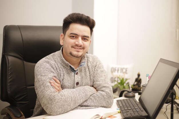 Um jovem empresário está sentado com os braços cruzados e sorrindo.