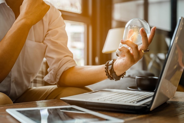 Um jovem empresário está trabalhando em uma cafeteria com um laptop, uma xícara de café e um tablet. O tubo vai representar a criatividade ou ideia.