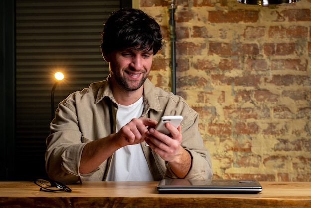 Um jovem empresário feliz está sorrindo usando um smartphone Retrato de um empresário sorridente lendo uma mensagem de um smartphone no escritório Um homem trabalhando em sua mesa no escritório