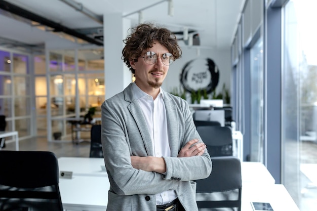 Um jovem empresário profissional com cabelos encaracolados está confiantemente num escritório bem iluminado.