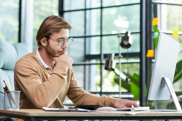 Um jovem empresário senta-se no escritório em uma mesa trabalha com documentos olha para notas em um caderno