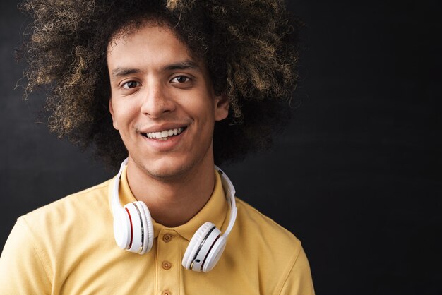 um jovem encaracolado alegre otimista adolescente posando sobre uma parede de lousa cinza com fones de ouvido.