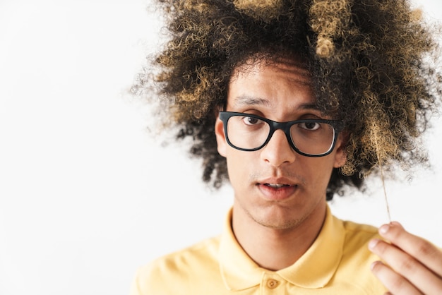 Foto um jovem encaracolado confuso isolado sobre uma parede branca, segurando o cabelo.