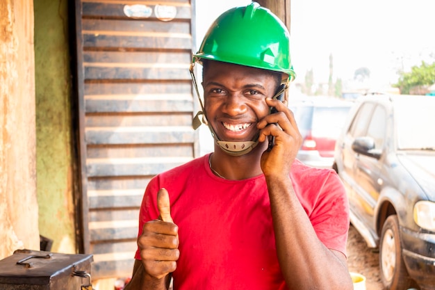 um jovem engenheiro africano fazendo um telefonema em seu local de trabalho e fez sinal de positivo.