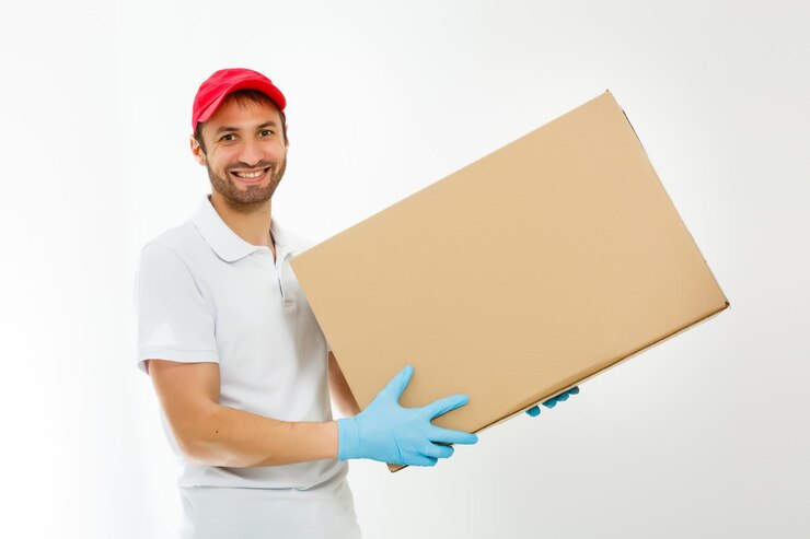 Foto um jovem entregador sorridente segurando e carregando uma caixa de cartão isolada em fundo branco