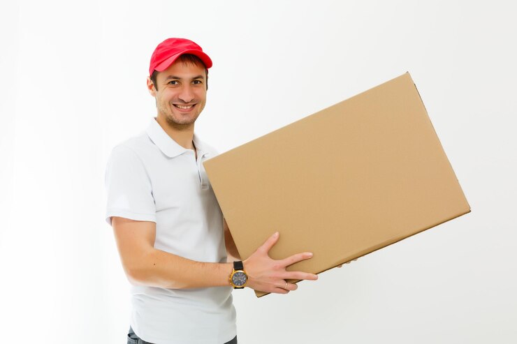 Foto um jovem entregador sorridente segurando e carregando uma caixa de cartão isolada em fundo branco