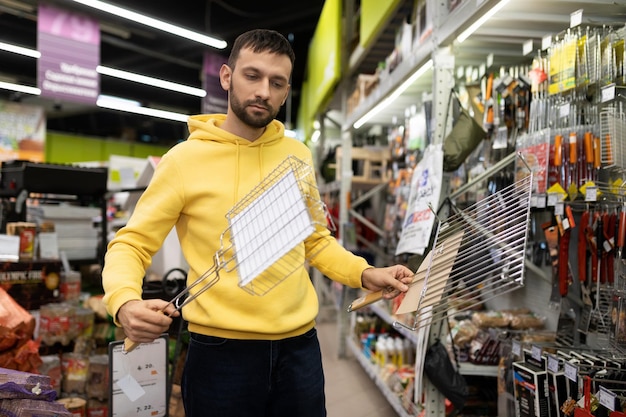 Um jovem escolhe uma grelha para um piquenique em uma loja de artigos turísticos