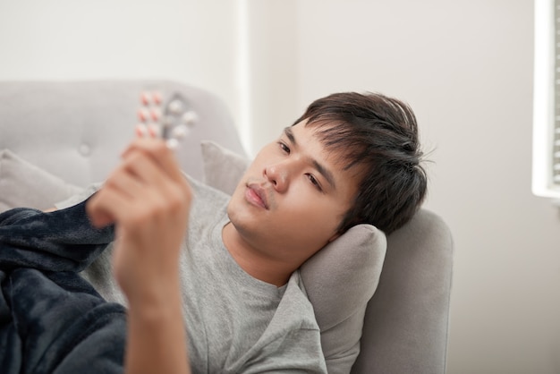 Um jovem está com gripe, deita-se em casa debaixo de um cobertor, toma um comprimido