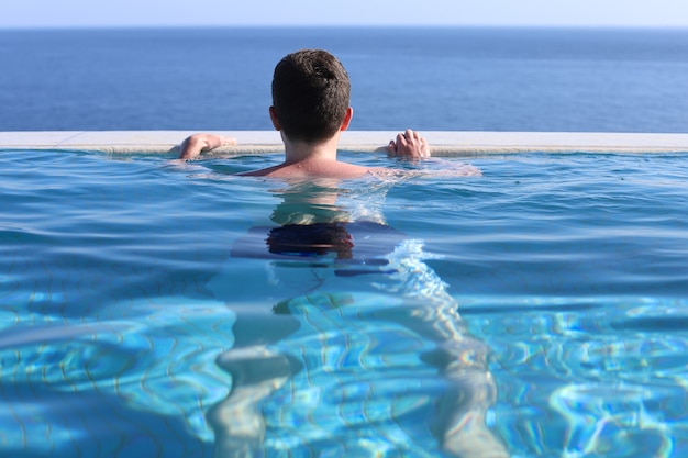 Um jovem está descansando à beira de uma piscina azul com vista para o mar