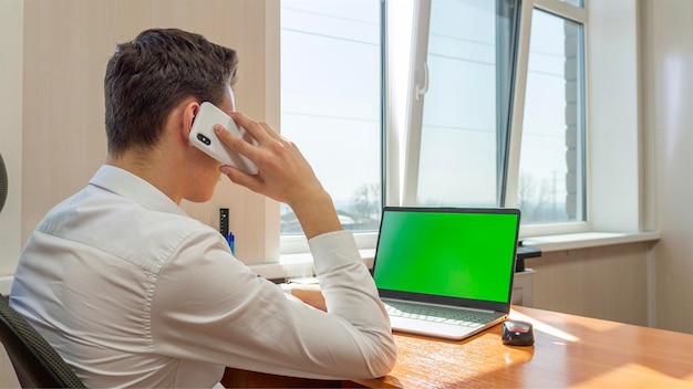 Um jovem está falando ao telefone na frente de um computador com tela verde