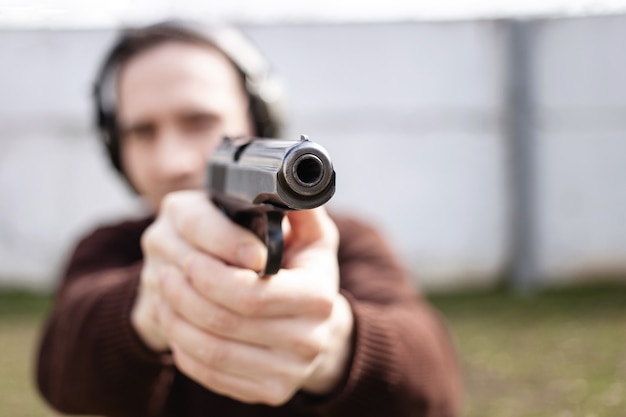 Um jovem está mirando em uma arma. Um homem usando fones de ouvido protetores.