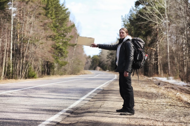 Um jovem está pedindo carona pelo país O homem está tentando pegar um carro que passa para viajar O homem com a mochila foi pedindo carona para o sul