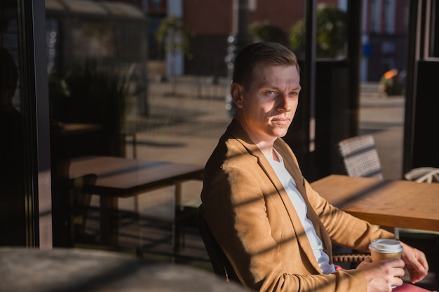 um jovem está sentado em um café esperando por uma reunião, bebendo café e pensando em algo