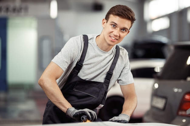 Um jovem está sorrindo enquanto polia um carro na manutenção de um veículo.