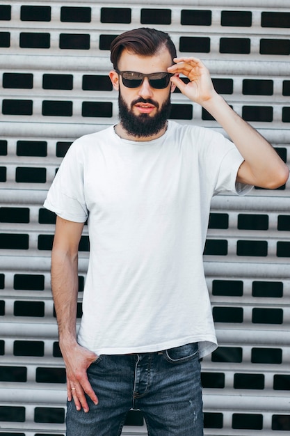 Um jovem estiloso com barba em uma camiseta branca e óculos. Foto de rua