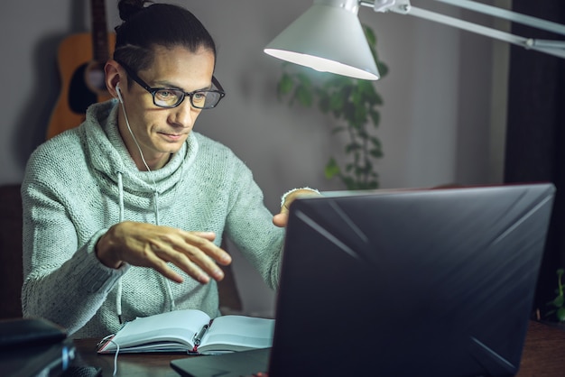 Foto um jovem estudante do sexo masculino está estudando em uma aula online usando um laptop à noite à luz de uma lâmpada na sala