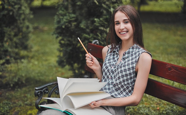 Um jovem estudante está sentado em um banco em um parque com um notebook e está pensando em algo