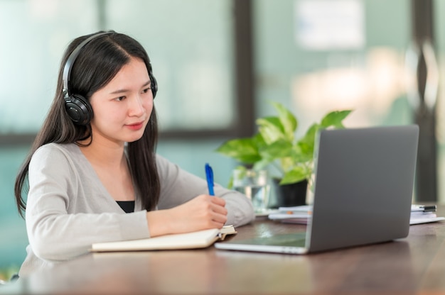 Um jovem estudante universitário asiático usando fones de ouvido para estudar online em casa, Durante o período do surto do vírus e não freqüentou a universidade.