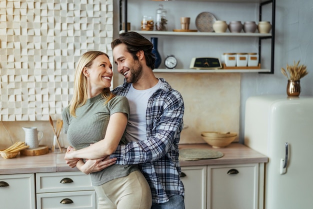 Um jovem europeu satisfeito abraçando sua esposa no relacionamento amoroso interior da cozinha moderna e