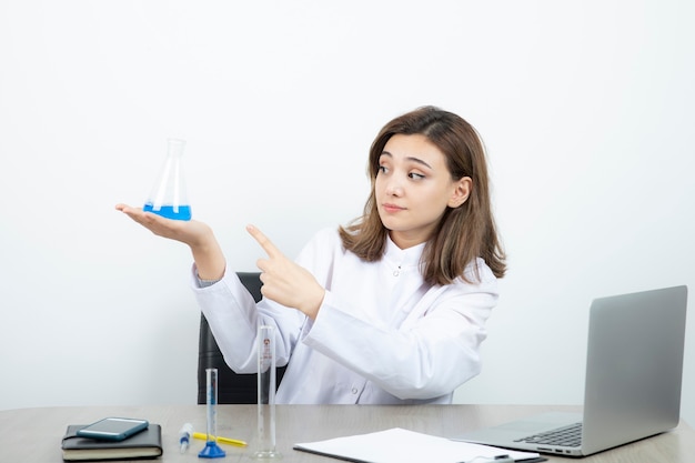 Um jovem farmacêutico de jaleco branco, apontando para o frasco de vidro com líquido.