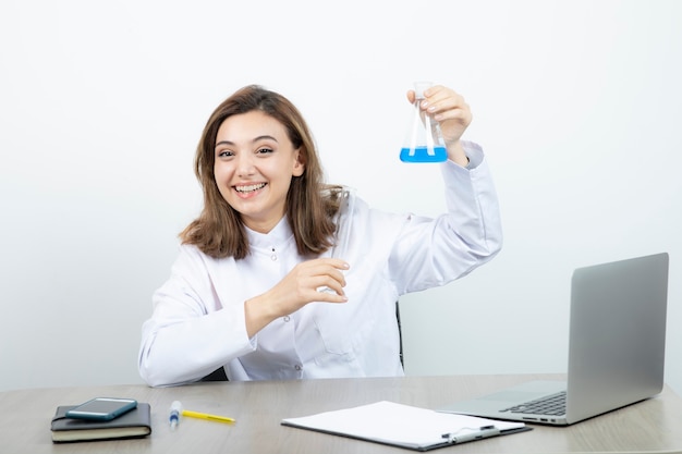 Um jovem farmacêutico de jaleco branco, segurando o frasco de vidro com líquido.