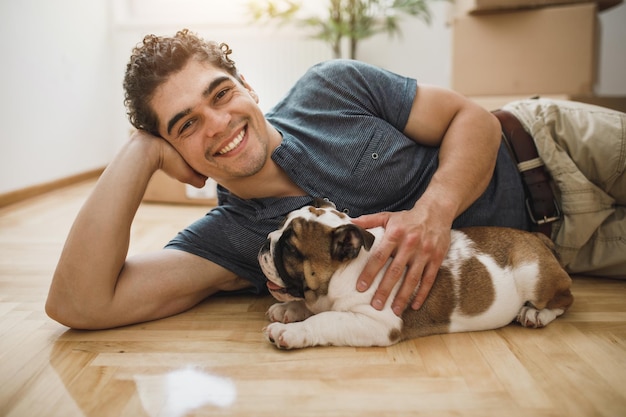 Um jovem feliz com seu filhote de bulldog inglês enquanto se muda para sua nova casa. olhando para a câmera.