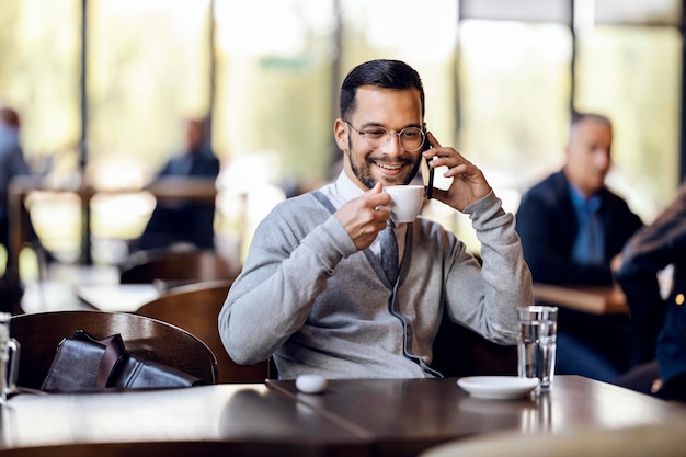 Um jovem feliz está falando ao telefone na cafeteria enquanto toma café