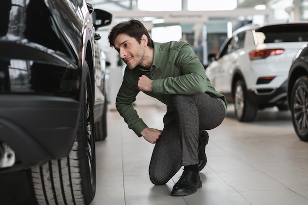 Um jovem feliz verificando um novo carro de luxo comprando automóvel no centro de concessionárias de comprimento total