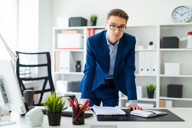 Um jovem fica no escritório, com as mãos na mesa.