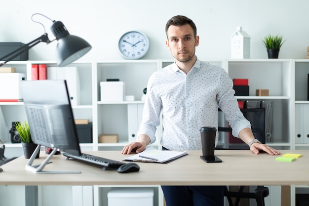 Foto um jovem fica perto de uma mesa no escritório