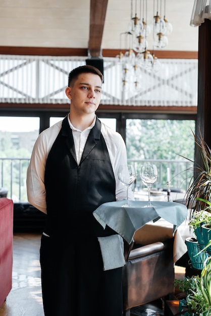 Foto um jovem garçom fica com taças de vinho em um restaurante moderno e elegante serviço de mesa no restaurante serviço e manutenção de alta cozinha