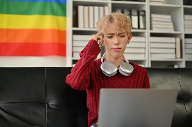 Um jovem gay asiático confuso está usando um laptop e tentando resolver o problema