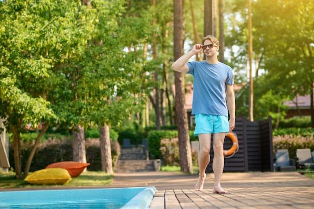 Um jovem homem. Um jovem com uma camiseta azul e óculos escuros perto da piscina