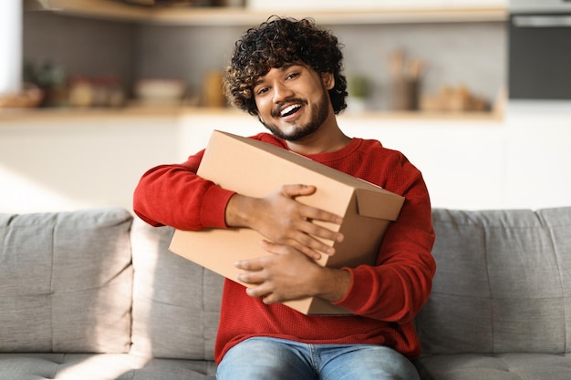 Um jovem indiano alegre abraçando uma grande caixa de papelão em casa.