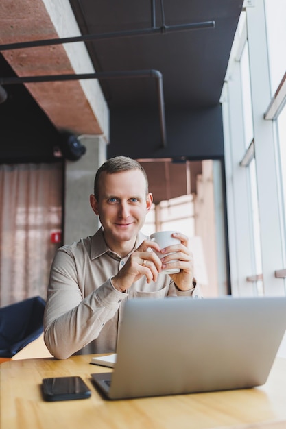 Um jovem inteligente está sentado no escritório com uma xícara de café e está trabalhando em um projeto relacionado à tecnologia cibernética pública Empresários com laptop tentando cumprir prazos em marketing externo