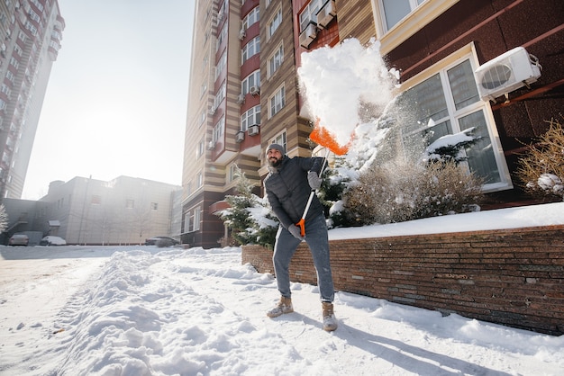 Um jovem limpa a neve na frente da casa em um dia ensolarado e gelado. limpando a rua da neve.