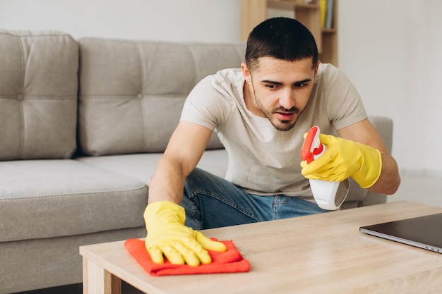 Um jovem limpa a sala de estar em casa limpa a mesa