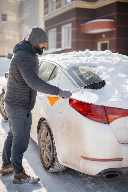 Um jovem limpa seu carro após uma nevasca em um dia ensolarado e gelado.