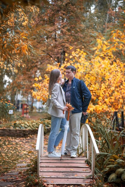 Um jovem lindo casal apaixonado vestido de estilo casual em um parque de outono fica em uma ponte de outono dourado