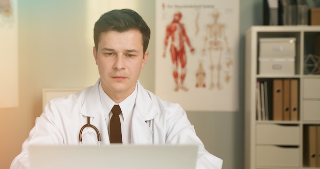 um jovem médico bonito com consulta on-line usando laptop