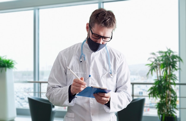 Um jovem médico de uniforme usando máscara protetora no hospital, clínica médica