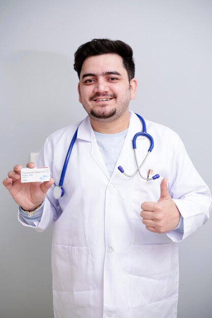 Foto um jovem médico está segurando o remédio em uma mão e mostrando o sinal de polegar para cima